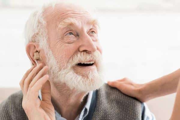 Senior man wearing hearing aid smiling up at someone 600x401 1