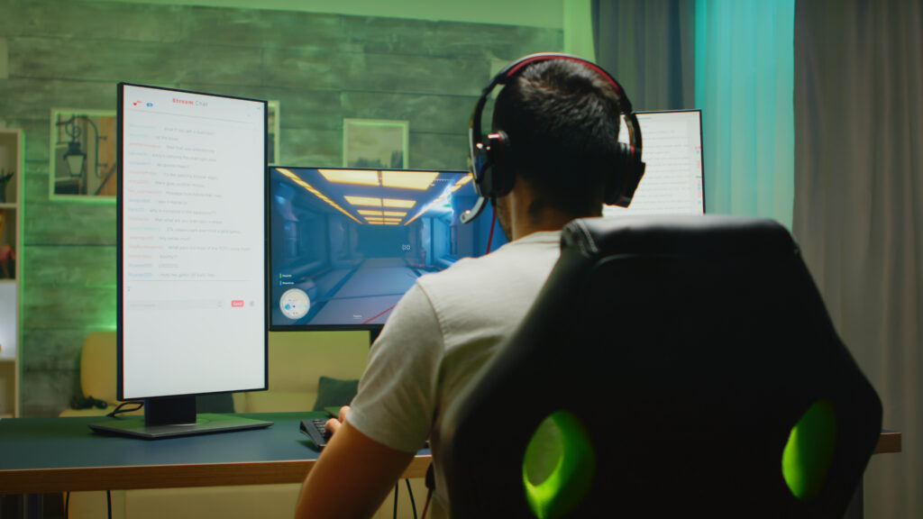 back view professional gamer streaming his competition triple monitor setup with two streaming chats open